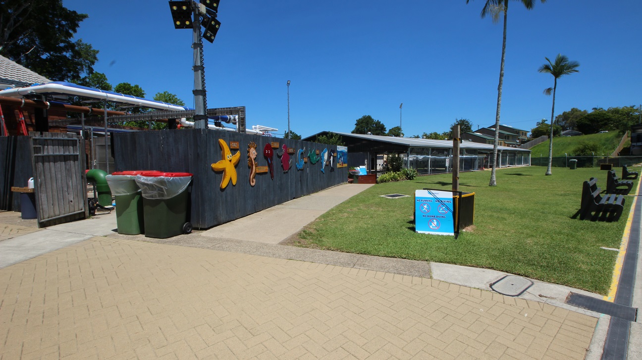 Access to the 25m Indoor Pool is down a slight step free ramp from the main 50m outdoor pool.  The concrete path is set next to a 2m dark blue fence on one side and a wide open grassed area to the right.