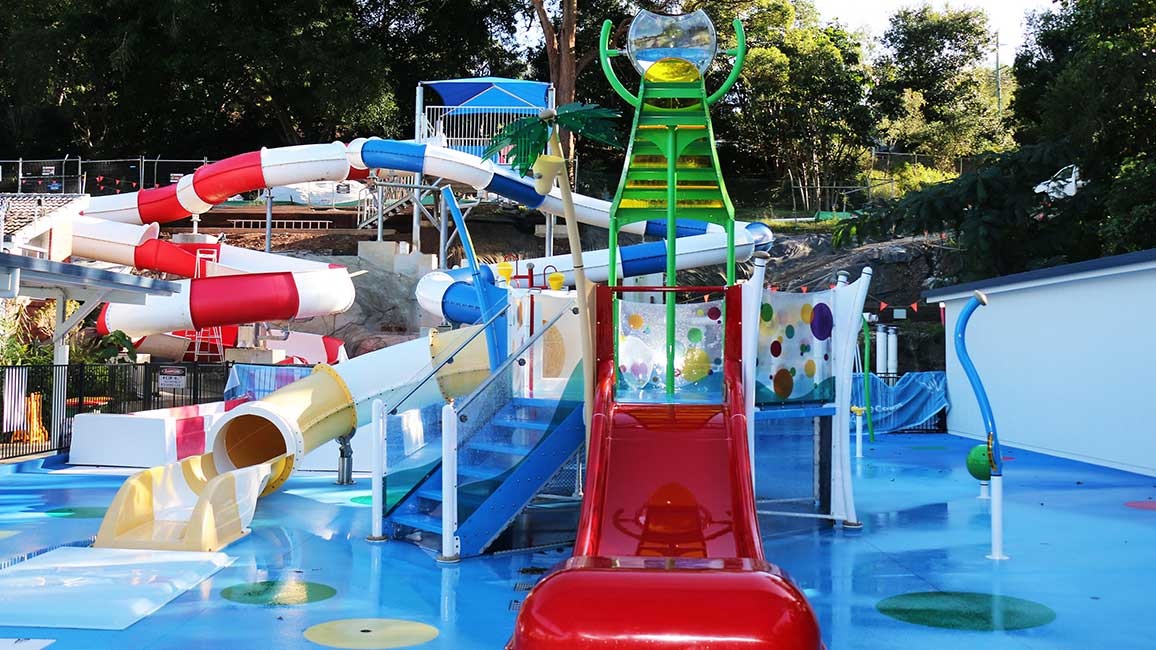 The Nambour Aquatic Centre Splash Park.  The aqua blue flooring is contrasted with the red slides and yellow and green equipment.