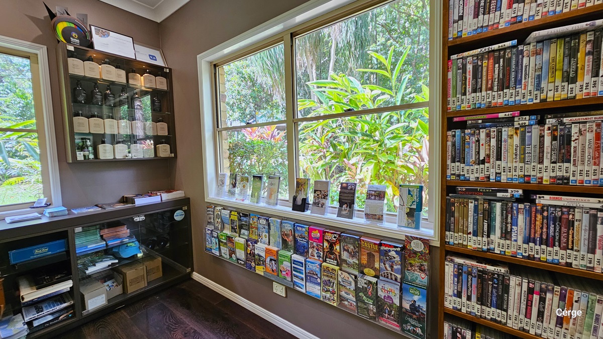 Upon arrival and turning right from the entrance at Narrows Escape Rainforest Retreat, you'll encounter a room featuring shelves filled with DVDs for rent, tourism information, retail items, and games available for borrowing, all neatly stacked. A large glass window on the right provides a view of the surroundings. In the corner, another shelf displays awards information. The floor is made of dark timber, complementing the vintage brown wall. Upon arrival and turning right from the entrance at Narrows Escape Rainforest Retreat, you'll encounter a room featuring shelves filled with DVDs for rent, tourism information, retail items, and games available for borrowing, all neatly stacked. A large glass window on the right provides a view of the surroundings. In the corner, another shelf displays awards information. The floor is made of dark timber, complementing the vintage brown wall.