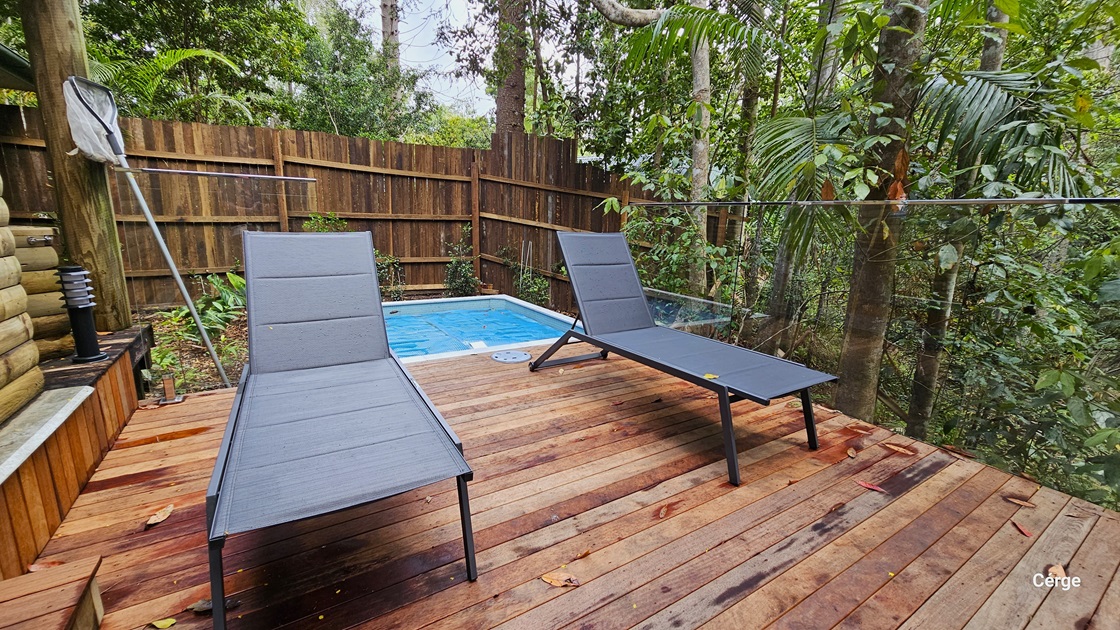 Accessing Kookaburra Cottage. The verandah features a small plunge pool in the end corner, accompanied by two black loungers. The area is secured by a steel fence, with a wooden plank fence providing additional privacy around the pool. The floor is made of timber, and on the left, there is a small lamp post. A leaf skimmer is leaning against a large post. Trees and vines surround the area. Accessing Kookaburra Cottage. The verandah features a small plunge pool in the end corner, accompanied by two black loungers. The area is secured by a steel fence, with a wooden plank fence providing additional privacy around the pool. The floor is made of timber, and on the left, there is a small lamp post. A leaf skimmer is leaning against a large post. Trees and vines surround the area.
