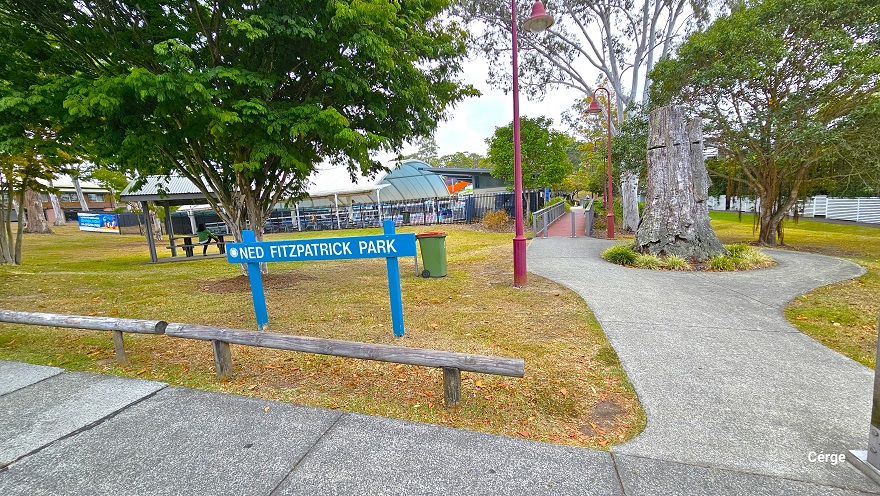 Arrival at Nerang Aquatic Centre from Cotton Street with a red brick road. This road is sloping downward with a number of designated car park spaces marked by white and yellow lines. On the right are residential buildings with similar designs and are enclosed by a white fence with trees. Tall trees with a large canopy cover surround the facility. The red bell-shaped lamp posts and a large white dome-shaped structure are evident from this position. Arrival at Nerang Aquatic Centre from Cotton Street with a red brick road. This road is sloping downward with a number of designated car park spaces marked by white and yellow lines. On the right are residential buildings with similar designs and are enclosed by a white fence with trees. Tall trees with a large canopy cover surround the facility. The red bell-shaped lamp posts and a large white dome-shaped structure are evident from this position.