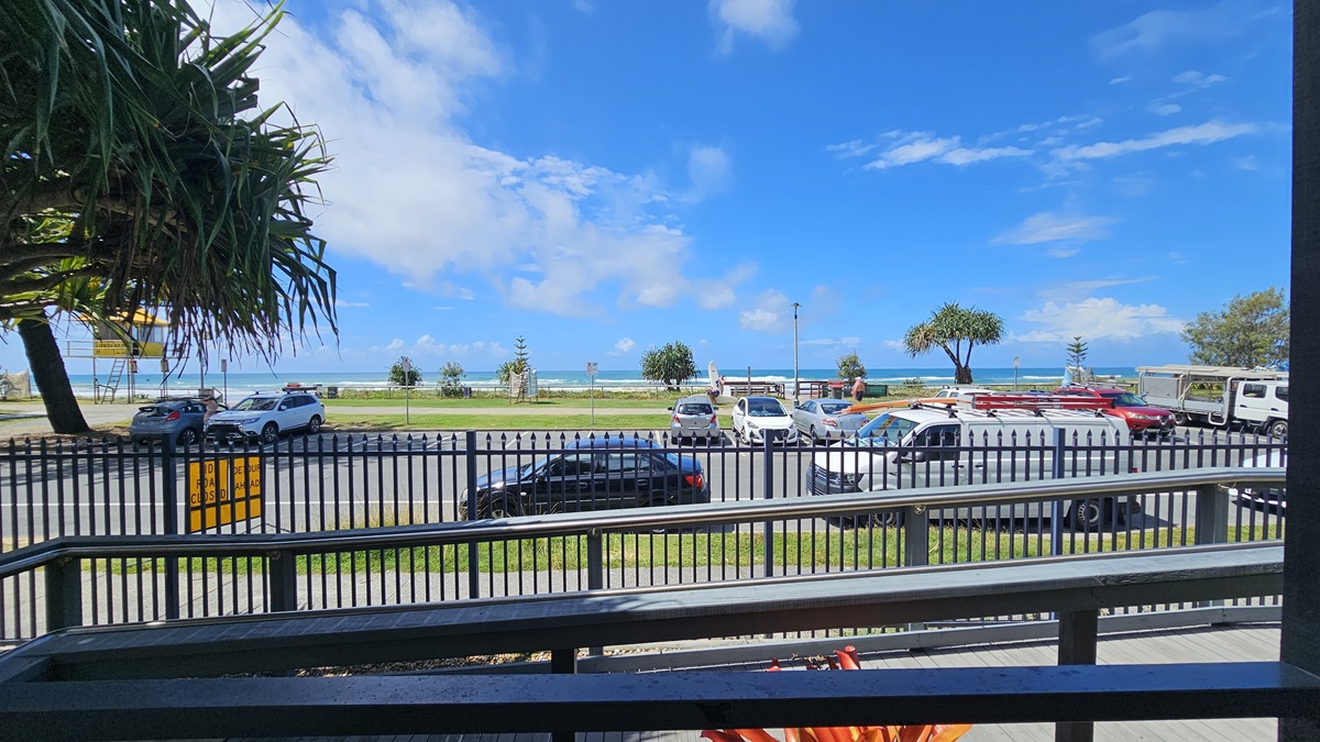 A concrete car park with several vehicles present. In the foreground, there is a ramp with handrails, which is secured by a metal fence. In the background, one can see the ocean and green grass. Additionally, a watchtower is visible on the left side of the image. Various trees and grass are also noticeable within the surroundings. A concrete car park with several vehicles present. In the foreground, there is a ramp with handrails, which is secured by a metal fence. In the background, one can see the ocean and green grass. Additionally, a watchtower is visible on the left side of the image. Various trees and grass are also noticeable within the surroundings.