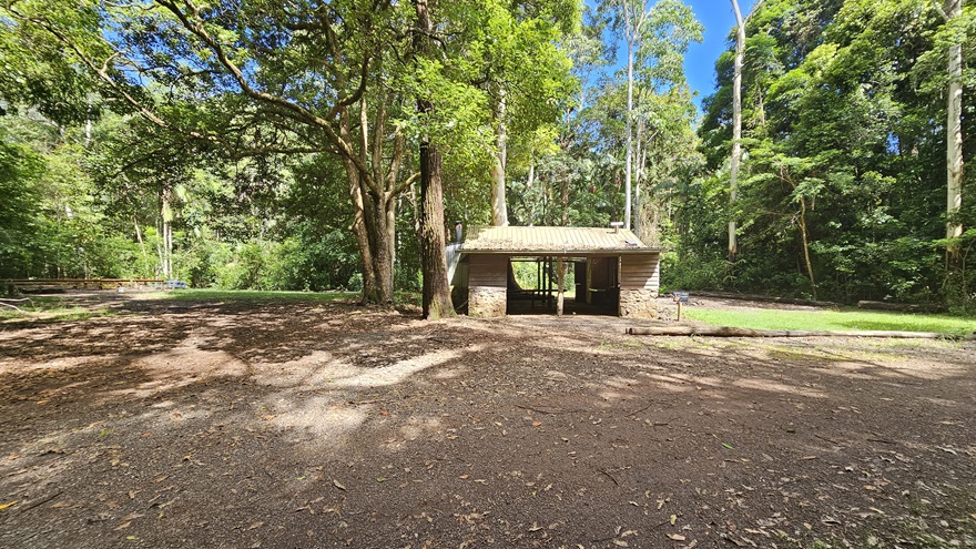 A straight unpaved dirt path leads to a hut. Native grass, shrubs, and tall trees border both sides of the pathway. A straight unpaved dirt path leads to a hut. Native grass, shrubs, and tall trees border both sides of the pathway.