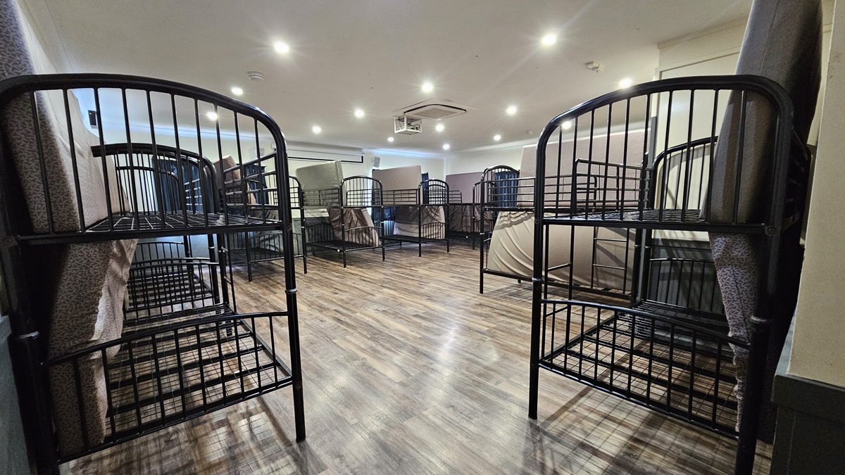A room with a brown timber floor featuring metal bunk beds strategically positioned against the walls. Each bed has mattresses laid at the sides. The white ceiling has LED lights and air conditioning, and the wall is white. A room with a brown timber floor featuring metal bunk beds strategically positioned against the walls. Each bed has mattresses laid at the sides. The white ceiling has LED lights and air conditioning, and the wall is white.