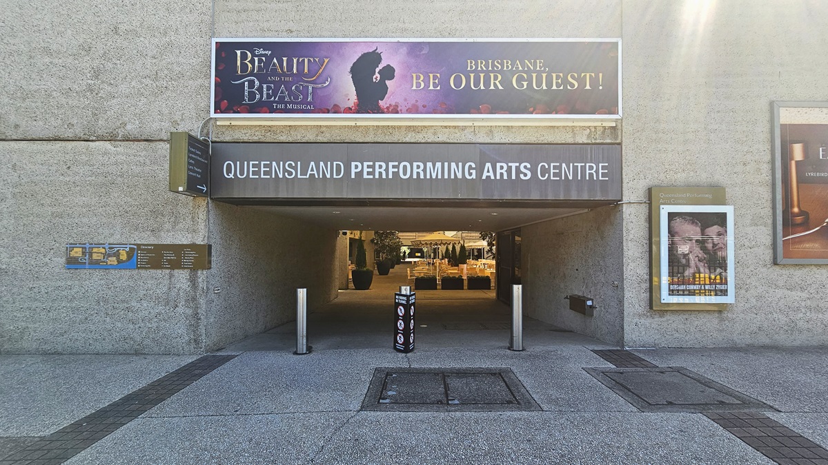 The tunnel features facility signage atop another signage. Additional directional signs and posters adorn the walls. Concrete bollards line the front. Inside, retail shops are visible. The building's front has a concrete facade with black tile flooring.