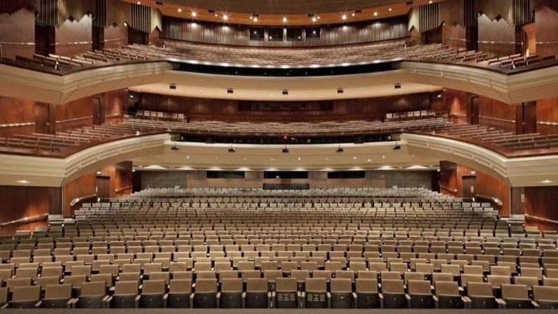 A panoramic view of the concert hall with seating arranged on the first, second, and third levels. The wall features a wooden structure.