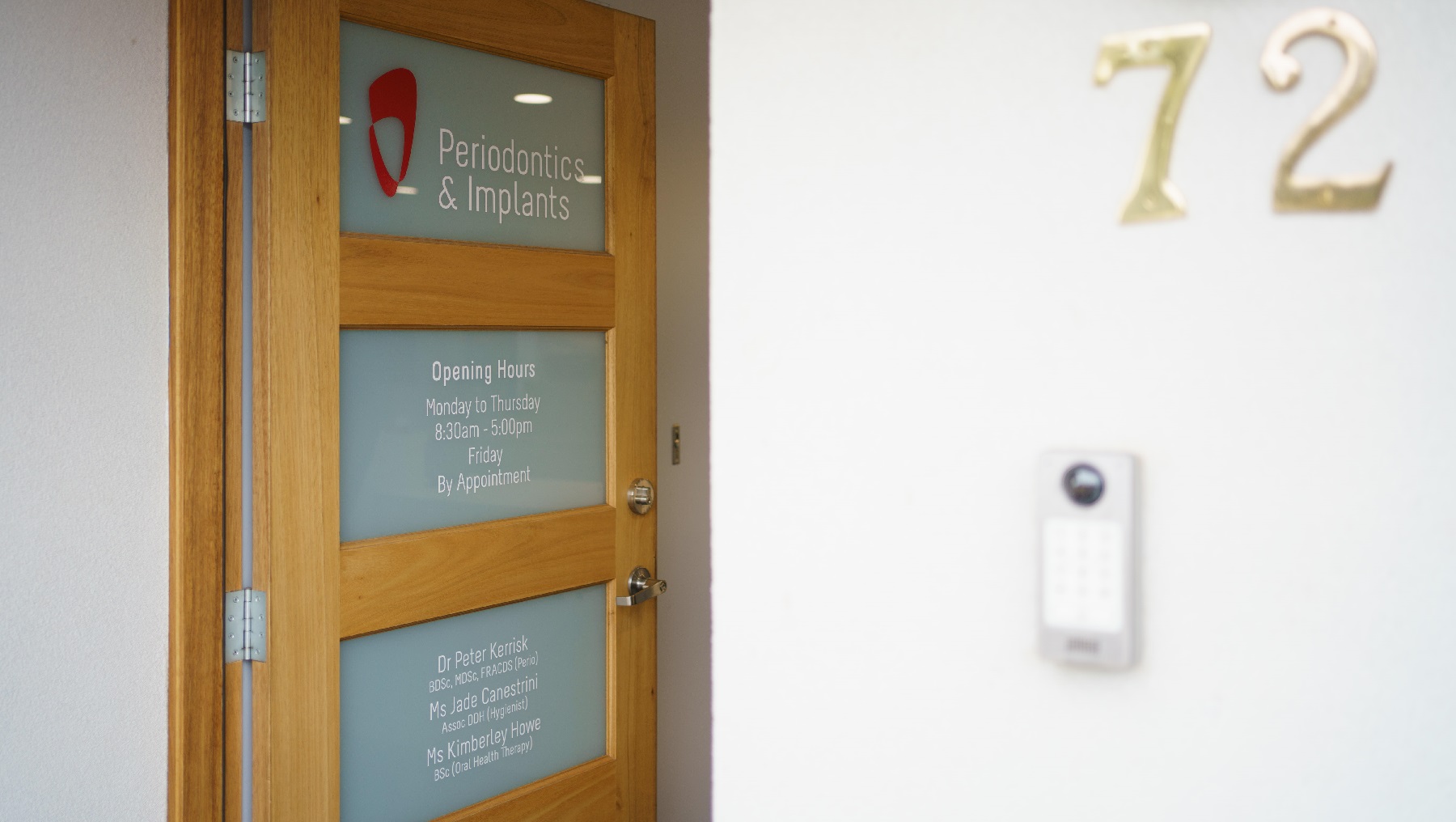 A close look of the front door open which is a timber door with three glass panels visible. The tope panel states 'Periodontics & Implants', the second panel down states the opening hours of Monday to Thursday of 8.30 am to 5pm and Friday by Appointment. The third panel down details the details of the dentist and assistants as well as their credentials. To the right is the number 12 with a door bell underneath this number. A close look of the front door open which is a timber door with three glass panels visible. The tope panel states 'Periodontics & Implants', the second panel down states the opening hours of Monday to Thursday of 8.30 am to 5pm and Friday by Appointment. The third panel down details the details of the dentist and assistants as well as their credentials. To the right is the number 12 with a door bell underneath this number.