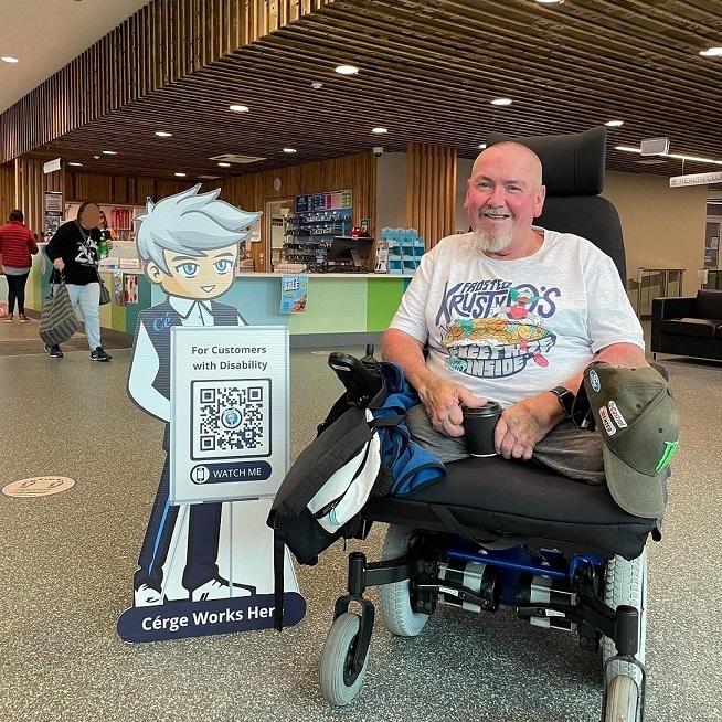 A man kneels beside a cartoon cutout with a QR sign at a pool facility.
