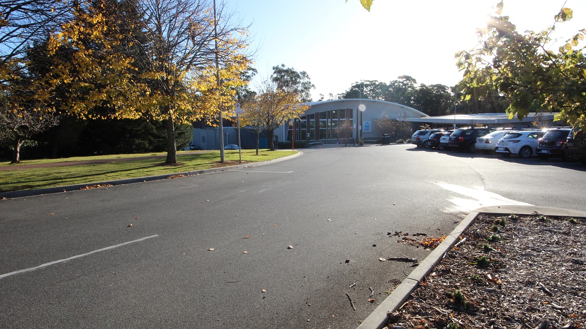 Road going to the Splash Devonport. On the right side is one of the accessible parking spaces near the entrance, while on the left side is a large space with Bermuda grass and trees with yellow leaves. Road going to the Splash Devonport. On the right side is one of the accessible parking spaces near the entrance, while on the left side is a large space with Bermuda grass and trees with yellow leaves.