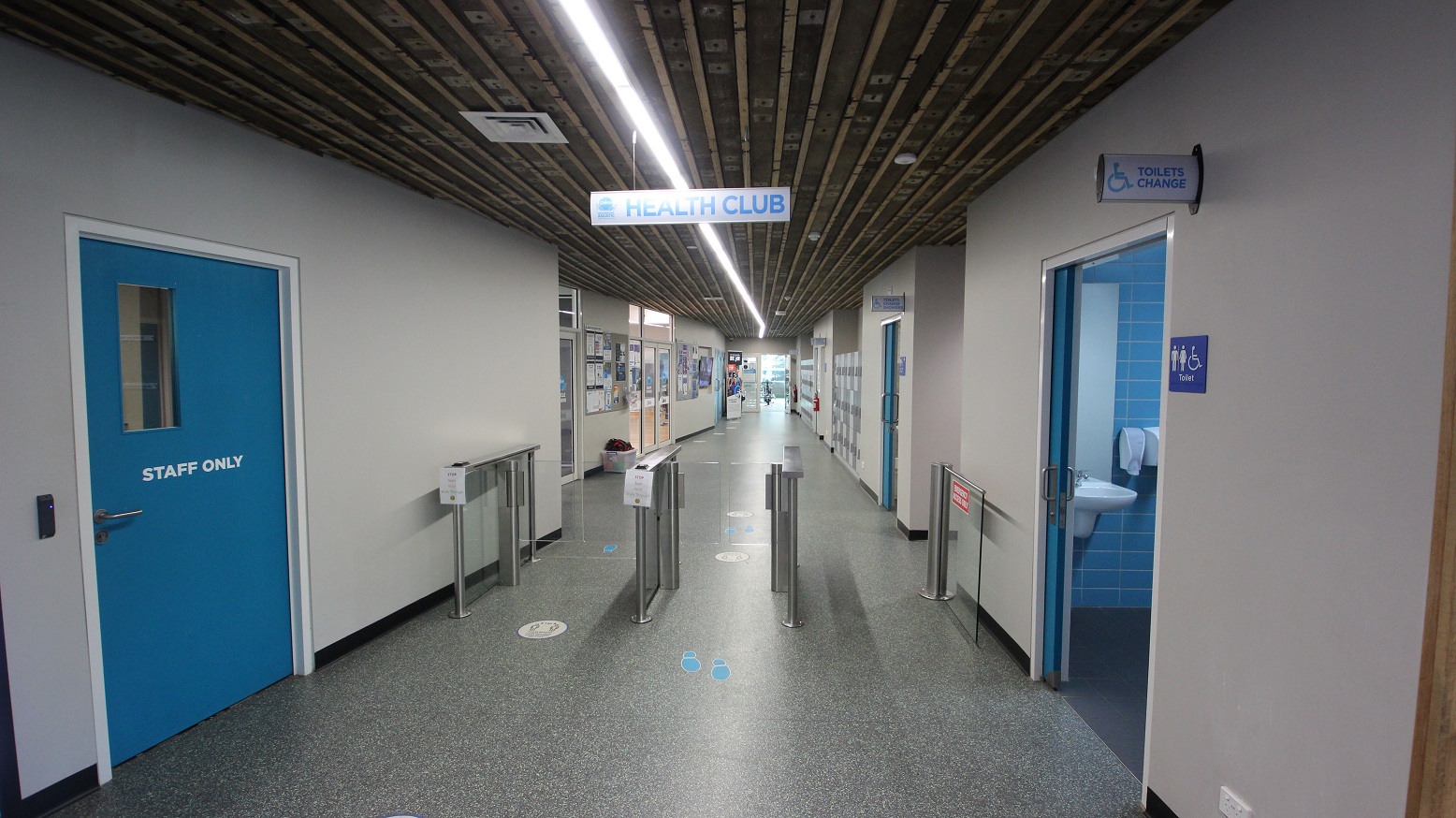 Turnstiles at the Health Club section at Splash Devonport. On the left side is the blue door with a metal handle with a staff-only label. To the right, is the Unisex Toilet Change area, which is designated by symbols for men, women, and people with mobility disabilities. Turnstiles at the Health Club section at Splash Devonport. On the left side is the blue door with a metal handle with a staff-only label. To the right, is the Unisex Toilet Change area, which is designated by symbols for men, women, and people with mobility disabilities.