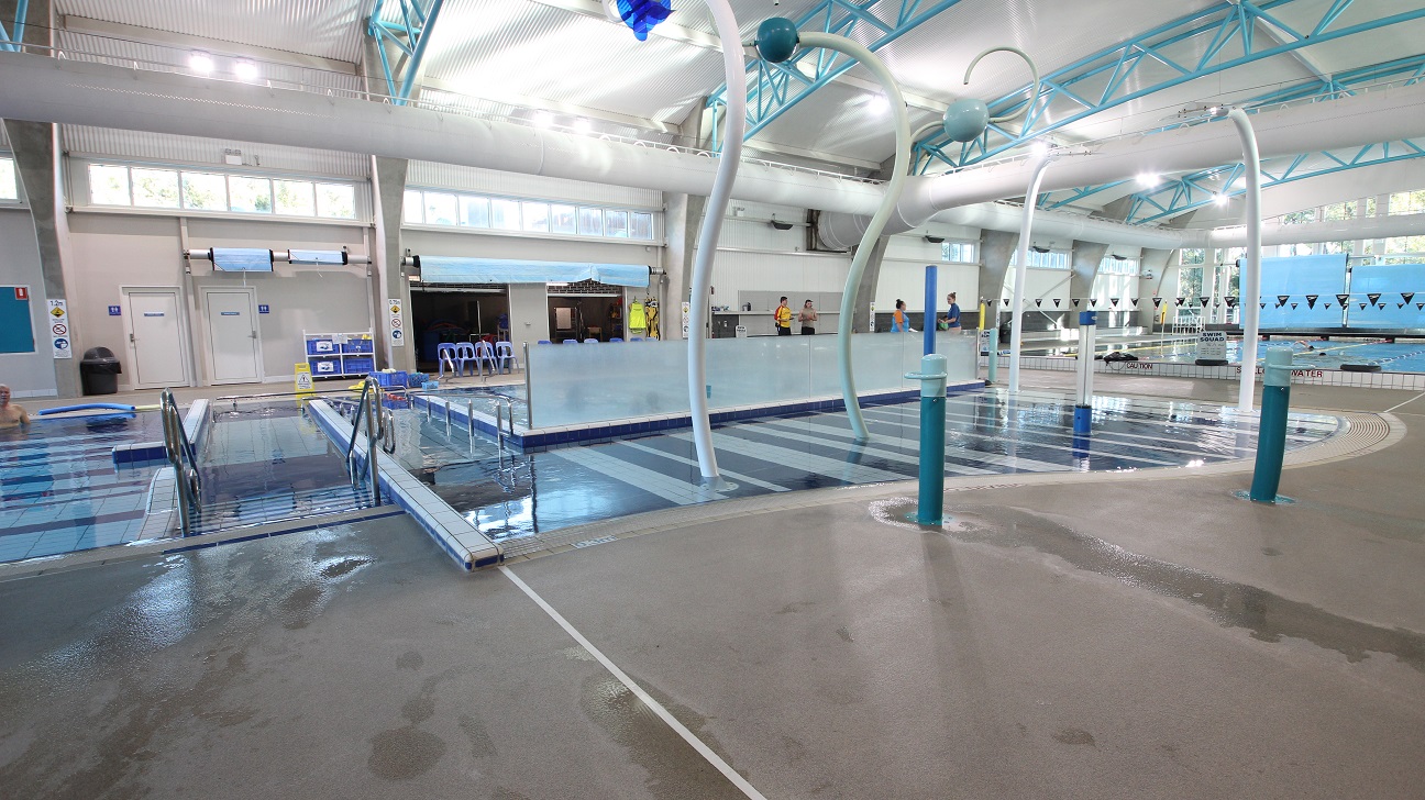 Automatic entrance doors at the Aquatic Centre in Splash Devonport. On the left side is the locker area with rectangular and square locker cabinets and their designated keys. The venue has very high ceilings with a corrugated iron finish and solid light blue steel archways. Large air conditioning white tubes dominate the ceiling space. Automatic entrance doors at the Aquatic Centre in Splash Devonport. On the left side is the locker area with rectangular and square locker cabinets and their designated keys. The venue has very high ceilings with a corrugated iron finish and solid light blue steel archways. Large air conditioning white tubes dominate the ceiling space.