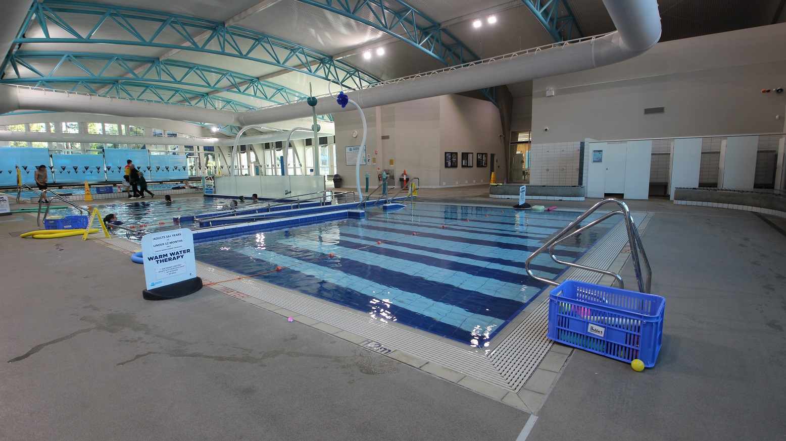 Learn to swim pool plus hydrotherapy or warm water therapy pool. The floor is made of granite floor tiles, and the walls are painted white. At the end of the image are several changing rooms, which can be accessed by turning left upon entering the entrance doors at the venue. Learn to swim pool plus hydrotherapy or warm water therapy pool. The floor is made of granite floor tiles, and the walls are painted white. At the end of the image are several changing rooms, which can be accessed by turning left upon entering the entrance doors at the venue.