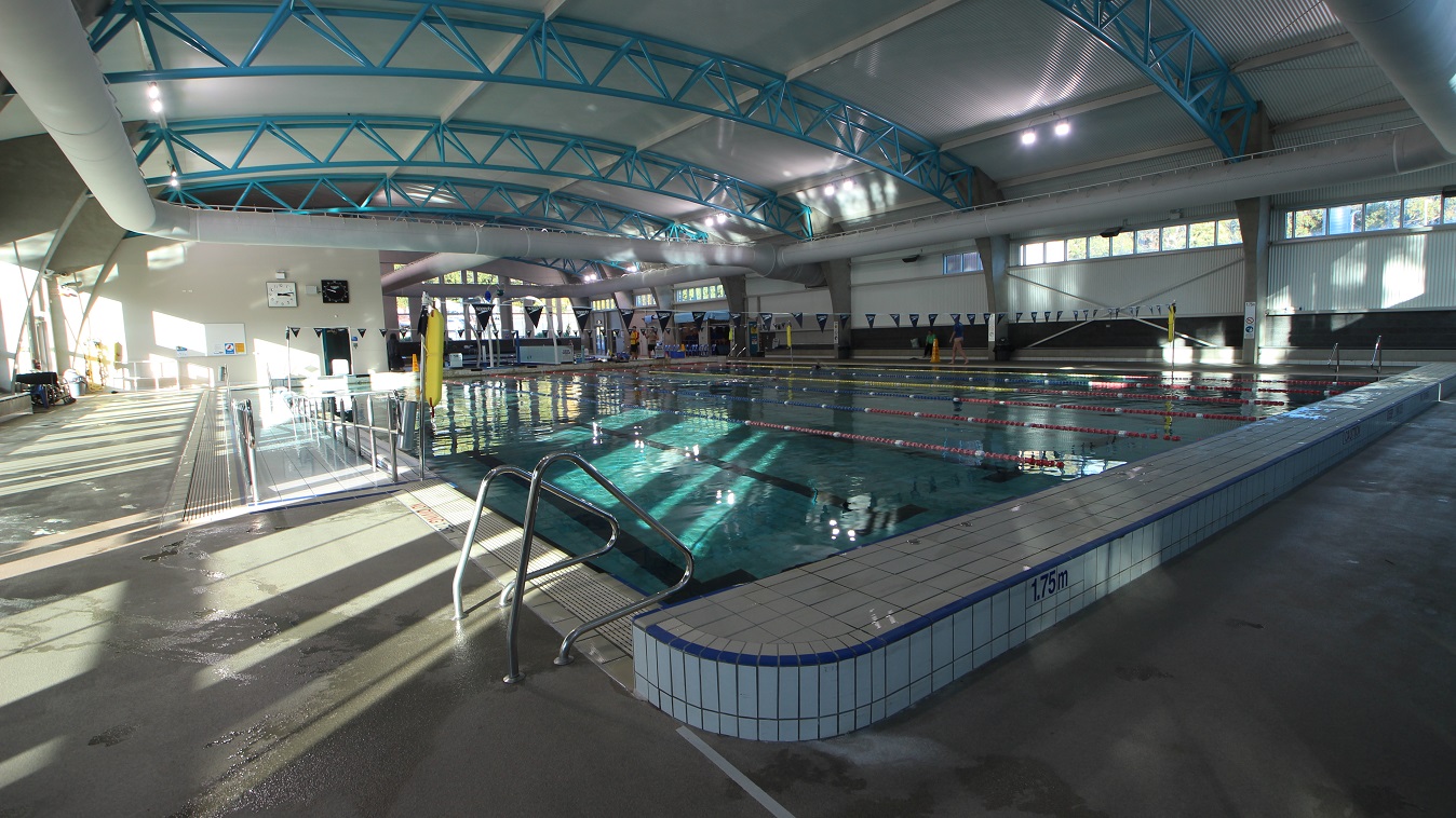 The 1.75-meter depth lane of the 25-meter pool in Splash Devonport aquatic centre. This side of the pool also has a staircase. Evident in this image are the high ceilings with a corrugated iron finish and solid light blue steel archways. Large air conditioning white tubes dominate the ceiling space. The 1.75-meter depth lane of the 25-meter pool in Splash Devonport aquatic centre. This side of the pool also has a staircase. Evident in this image are the high ceilings with a corrugated iron finish and solid light blue steel archways. Large air conditioning white tubes dominate the ceiling space.
