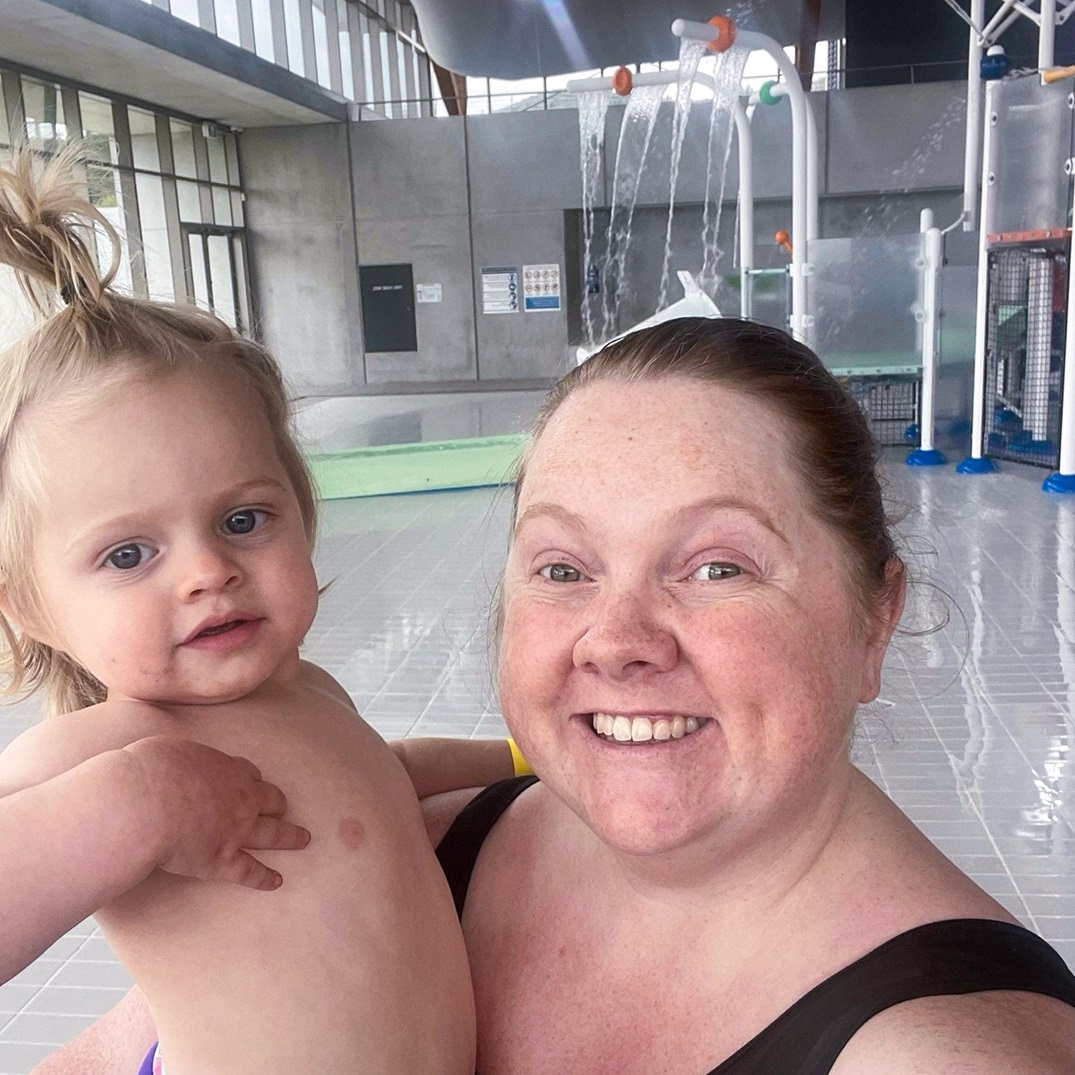 A smiling woman holds a baby in a bright indoor pool area. A smiling woman holds a baby in a bright indoor pool area.