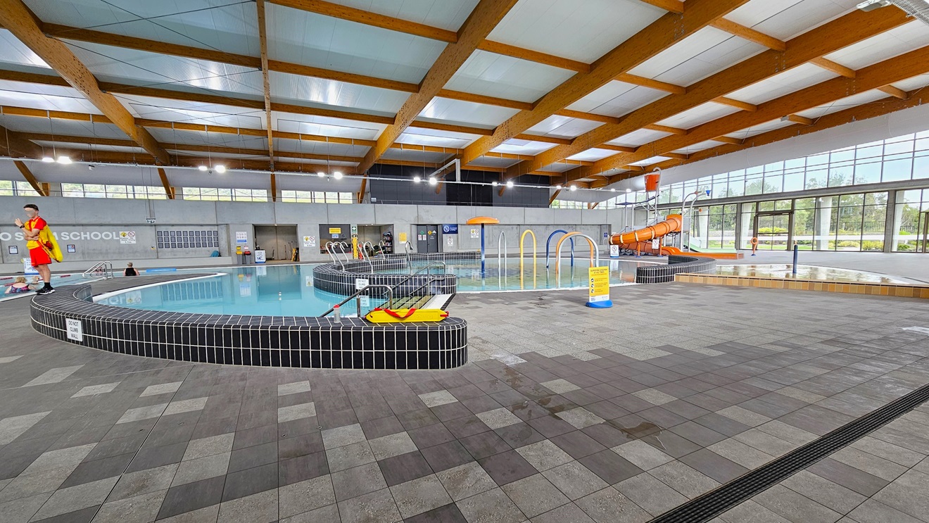 The entryway to the Indoor Aquatic Center features an automated glass sliding door adorned with three posters and a sticker accent. A sign is attached to the upper left wall. The exterior wall is constructed of grey bricks, while the floor is covered with grey tiles. The ceiling is uniformly white. Posters are displayed on the glass wall. The entryway to the Indoor Aquatic Center features an automated glass sliding door adorned with three posters and a sticker accent. A sign is attached to the upper left wall. The exterior wall is constructed of grey bricks, while the floor is covered with grey tiles. The ceiling is uniformly white. Posters are displayed on the glass wall.