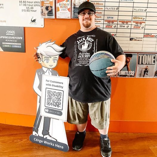A man in a black shirt and shorts stands beside a cartoon cutout with a QR sign and a basketball. A man in a black shirt and shorts stands beside a cartoon cutout with a QR sign and a basketball.
