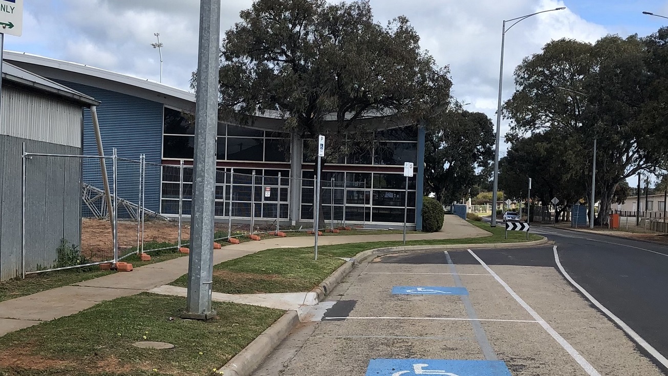 This is the other side of Swan Hill Leisure Centre that’s close to the main road. It has a white pavement leading to the entrance door. There are also several accessible car spaces. From this view, you will see the tall trees and street signs. There is also an unfinished fence being built that has silver line posts without the chain wire. This is the other side of Swan Hill Leisure Centre that’s close to the main road. It has a white pavement leading to the entrance door. There are also several accessible car spaces. From this view, you will see the tall trees and street signs. There is also an unfinished fence being built that has silver line posts without the chain wire.