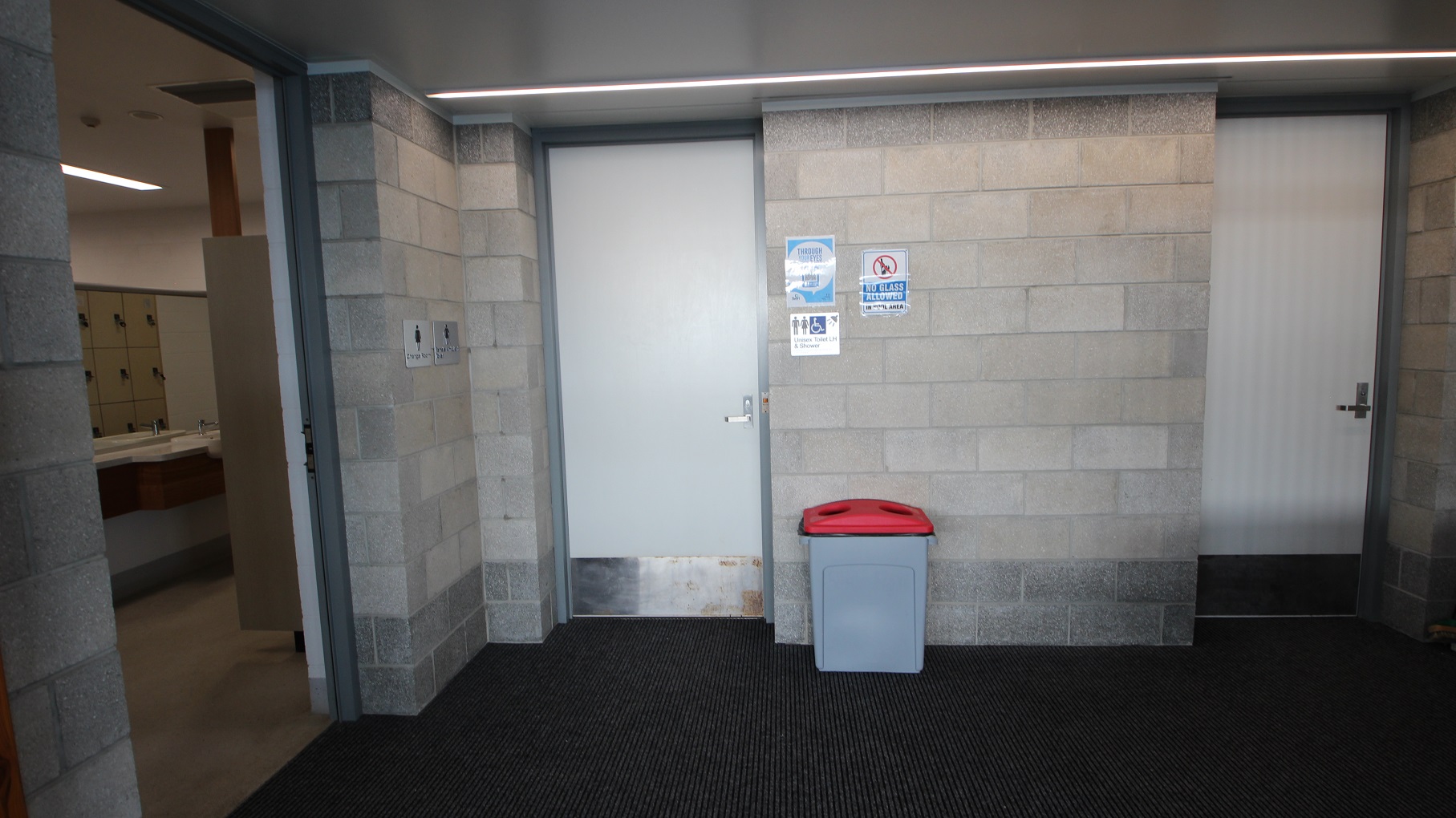Unisex toilet and shower at SWIRL. A no glass allowed sign can be seen on the grey brick wall on the right side of the door. A grey rubbish bin with a red lid can be seen right outside the unisex toilet and shower room. Adjacent is an open door for toilets. Unisex toilet and shower at SWIRL. A no glass allowed sign can be seen on the grey brick wall on the right side of the door. A grey rubbish bin with a red lid can be seen right outside the unisex toilet and shower room. Adjacent is an open door for toilets.