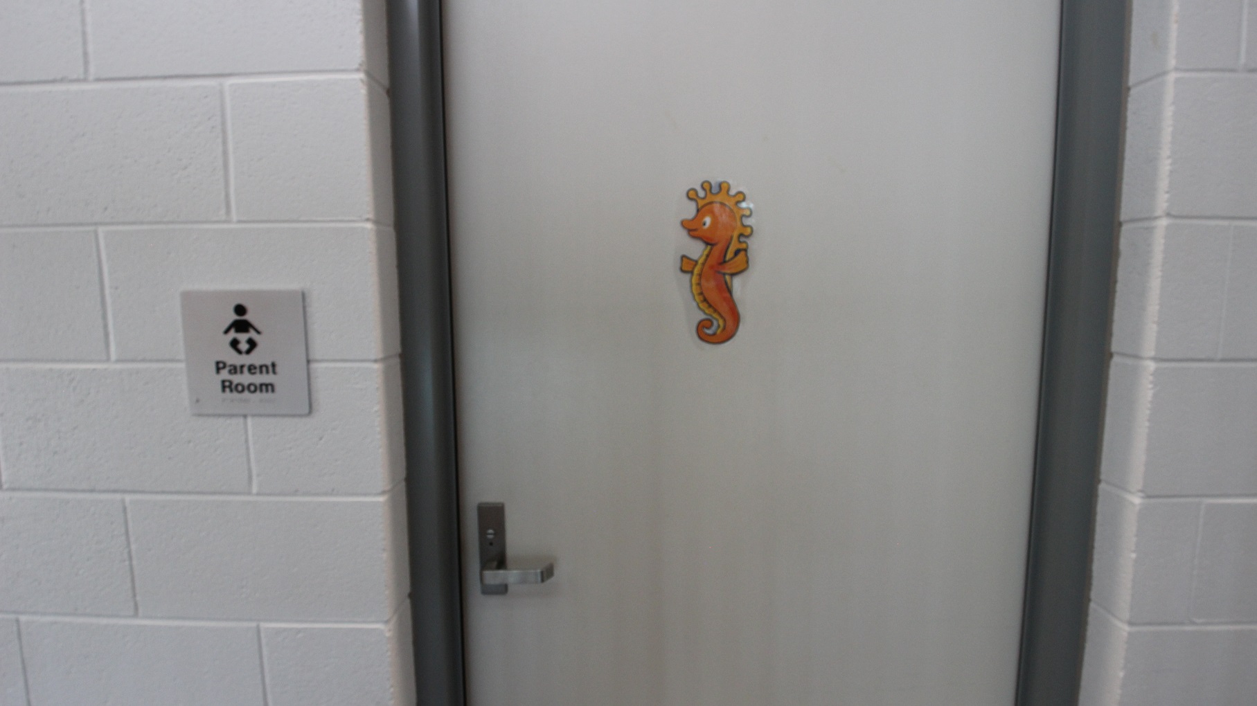 Parent room at SWIRL. It can be distinguished by the cute orange seahorse in the middle of the door and a white-painted brick wall. The door has a metal handle. Parent room at SWIRL. It can be distinguished by the cute orange seahorse in the middle of the door and a white-painted brick wall. The door has a metal handle.