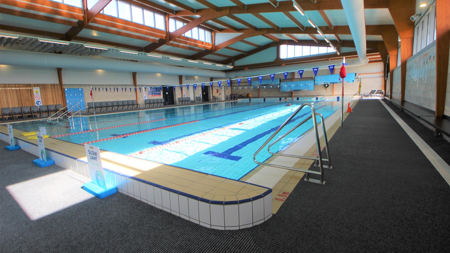 Opposite side of the stair entrance of the 25-metre indoor pool at SWIRL. There is a pool ladder on this side and white sign boards for the slow lane, medium lane, and fast lanes of the pool. Mounted on the white tiled wall on the right is a black seating platform. Opposite side of the stair entrance of the 25-metre indoor pool at SWIRL. There is a pool ladder on this side and white sign boards for the slow lane, medium lane, and fast lanes of the pool. Mounted on the white tiled wall on the right is a black seating platform.