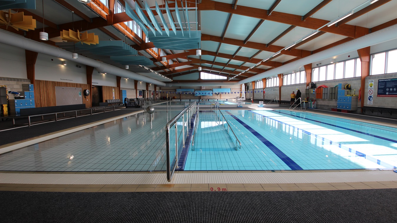 Central view of the three-lane (6 m x 12.5m) program pool and the shallow pool found near the entrance door is a steel frame with a glass wall. There are blue locker cabinets placed against the wall and grey-orange storage cabinets for bags mounted on the right of the three-lane pool. Central view of the three-lane (6 m x 12.5m) program pool and the shallow pool found near the entrance door is a steel frame with a glass wall. There are blue locker cabinets placed against the wall and grey-orange storage cabinets for bags mounted on the right of the three-lane pool.