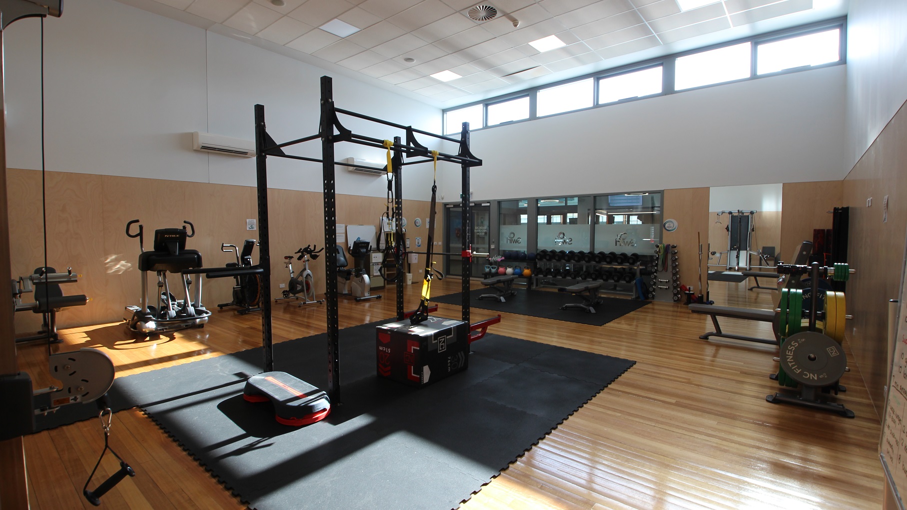 The timber floor inside the gym of SWIRL is well polished. The gym has a chic-vibe design with wood-like brown and white painted walls. The ceiling is composed of a small rectangular design that is painted in white. Found inside the gym are kettlebells, black adjustable professional gym benches, treadmills, bicycles, and a multi-functional squat power rack. There is a large mirror at the back, and some floor areas are covered by large black mats. The timber floor inside the gym of SWIRL is well polished. The gym has a chic-vibe design with wood-like brown and white painted walls. The ceiling is composed of a small rectangular design that is painted in white. Found inside the gym are kettlebells, black adjustable professional gym benches, treadmills, bicycles, and a multi-functional squat power rack. There is a large mirror at the back, and some floor areas are covered by large black mats.