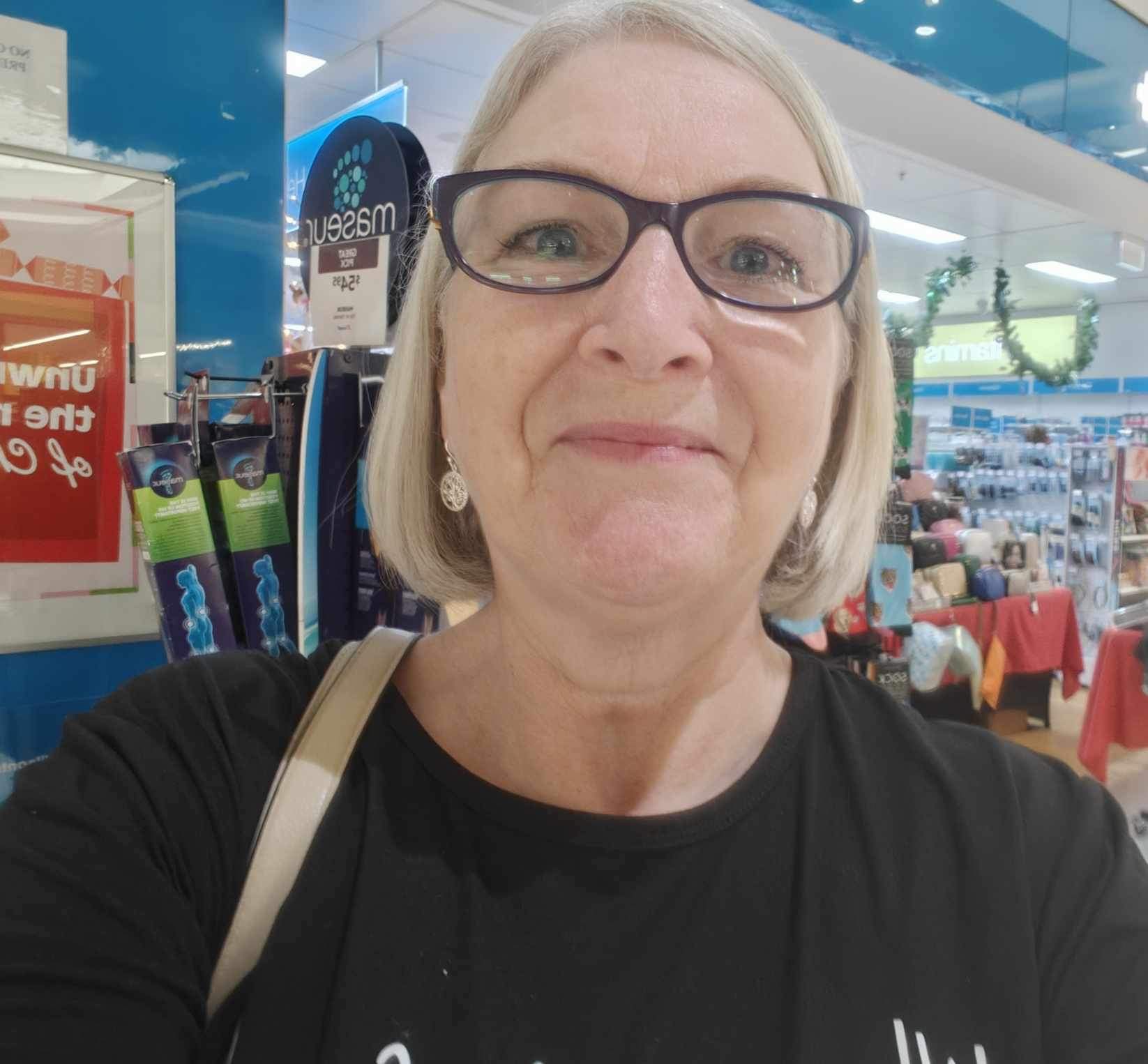 A woman with short hair and glasses stands in front of a pharmacy. A woman with short hair and glasses stands in front of a pharmacy.
