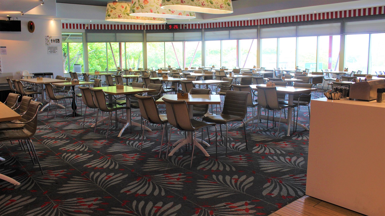 A dining hall at the Bistro restaurant covered with grey and crimson designed tiles. Having four seats to a table set vertically across the hall. In a corner, a timer is seen overlooking the white wall with a screen, an alarm and an infographic. Red stripes are seen across. In the centre, flowering white light covers dangle from the roof. A checking counter can be seen to the left of the entryway. The windows provide a glimpse of the outer world. A dining hall at the Bistro restaurant covered with grey and crimson designed tiles. Having four seats to a table set vertically across the hall. In a corner, a timer is seen overlooking the white wall with a screen, an alarm and an infographic. Red stripes are seen across. In the centre, flowering white light covers dangle from the roof. A checking counter can be seen to the left of the entryway. The windows provide a glimpse of the outer world.