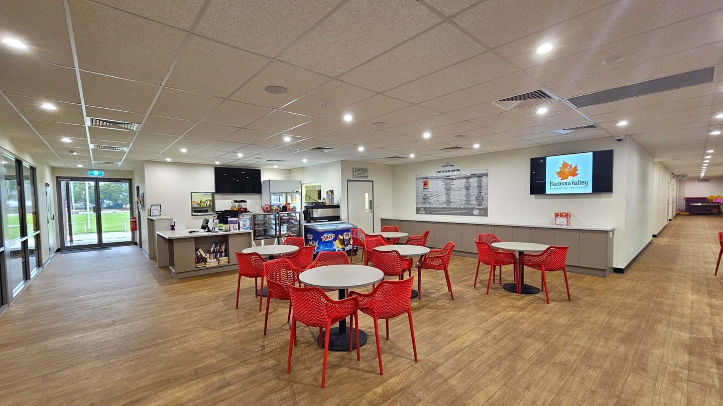 Upon entering, to the left is a floor-to-ceiling glass bearing the facility banner. A free-standing sign is also placed near the wall along with a rubbish bin. To the right is a white wall with a framed poster. Next to it is the court, also equipped with large floor-to-ceiling windows. Further in, there are red movable chairs and white tables arranged. A poster and a flat-screen TV are mounted on the middle wall. The floor is made of timber, and the ceiling is white with a porous design. Upon entering, to the left is a floor-to-ceiling glass bearing the facility banner. A free-standing sign is also placed near the wall along with a rubbish bin. To the right is a white wall with a framed poster. Next to it is the court, also equipped with large floor-to-ceiling windows. Further in, there are red movable chairs and white tables arranged. A poster and a flat-screen TV are mounted on the middle wall. The floor is made of timber, and the ceiling is white with a porous design.