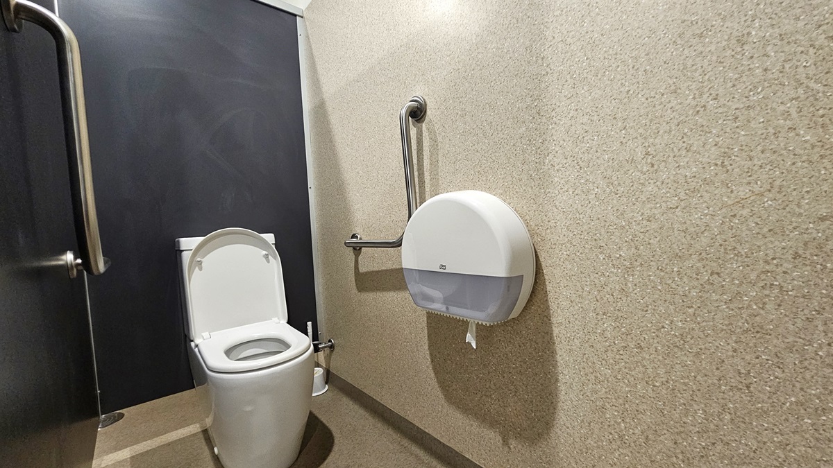 A white toilet bowl is positioned in the corner, accompanied by stainless steel handrails on both sides of the wall, along with a tissue dispenser. The left and middle walls are constructed of black granite, while the right wall is made of brown granite. The floor area is also covered in brown granite. A white toilet bowl is positioned in the corner, accompanied by stainless steel handrails on both sides of the wall, along with a tissue dispenser. The left and middle walls are constructed of black granite, while the right wall is made of brown granite. The floor area is also covered in brown granite.