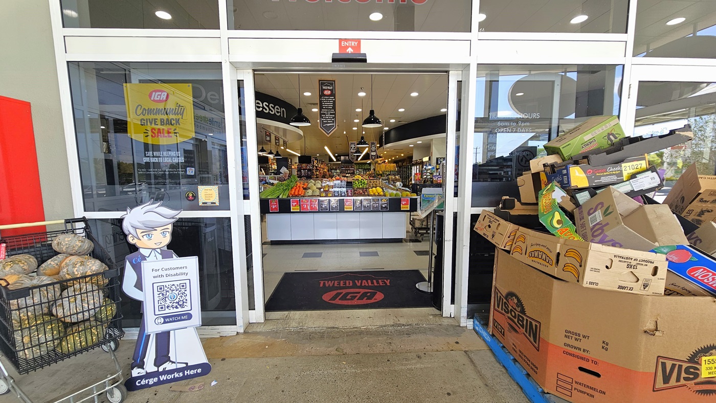 Entrance of the Tweed Valley IGA building. A black doormat with the building’s name and icon is visible. A well-organized display of fruits and vegetables is situated at the entrance upon entering. Fluorescent lights and hanging banners clearly dominate the ceiling of the building. Entrance of the Tweed Valley IGA building. A black doormat with the building’s name and icon is visible. A well-organized display of fruits and vegetables is situated at the entrance upon entering. Fluorescent lights and hanging banners clearly dominate the ceiling of the building.