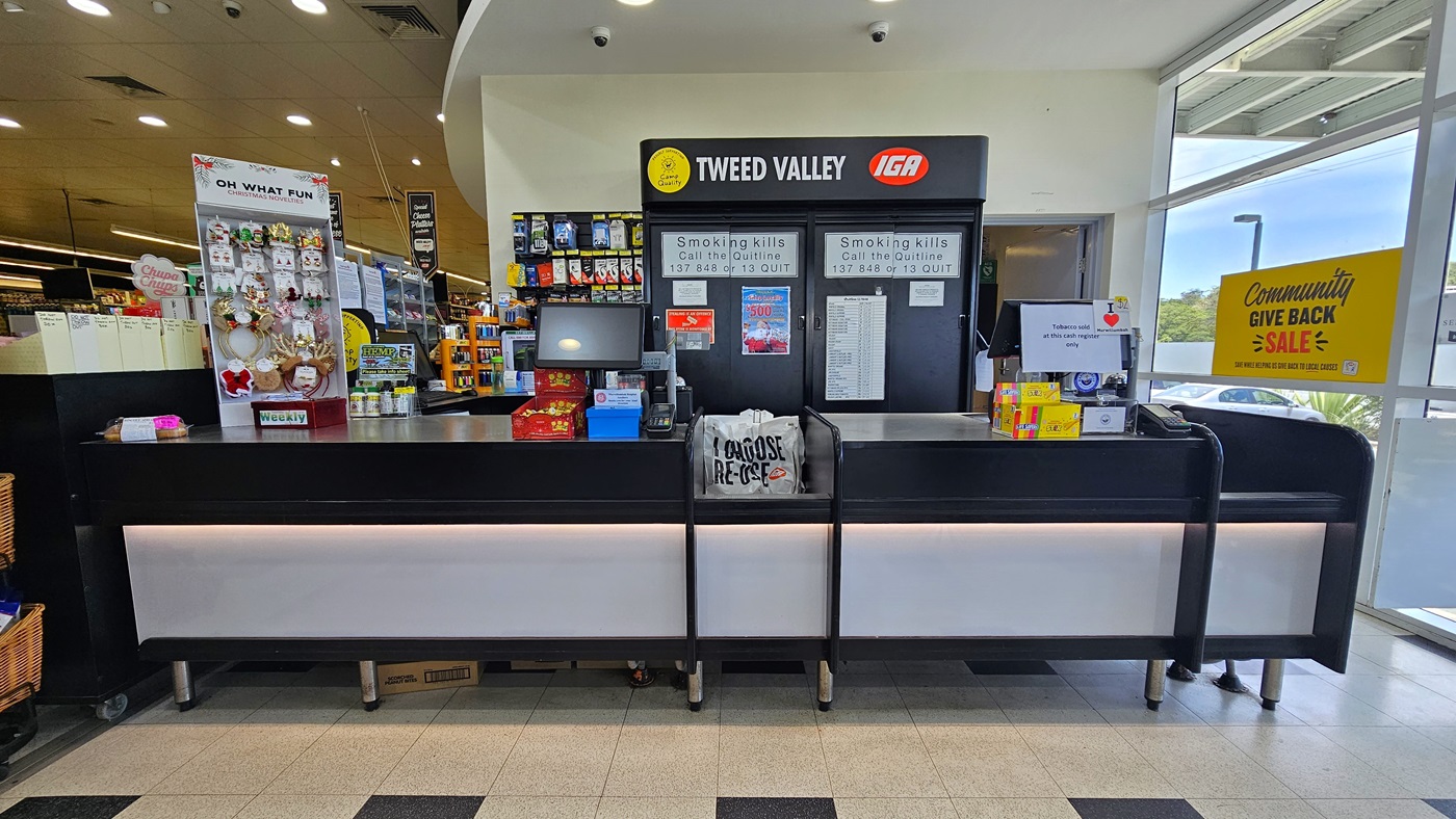 Checkout area near the entrance of the building. On the left, a multi-layer rack full of chips and other products is visible beside three piled-up wooden baskets with chips. Two counters are also visible on the left, with three checkout staff members noticeable. On top of the employee's left, there are two functional CCTVs. On the right, there are also three wooden baskets with chips and a fridge full of soft drinks, where several water bottles sit atop. Checkout area near the entrance of the building. On the left, a multi-layer rack full of chips and other products is visible beside three piled-up wooden baskets with chips. Two counters are also visible on the left, with three checkout staff members noticeable. On top of the employee's left, there are two functional CCTVs. On the right, there are also three wooden baskets with chips and a fridge full of soft drinks, where several water bottles sit atop.