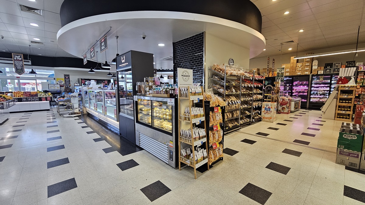Rear view of the Delicatessen section. Multi-layer racks filled with grocery items such as chips, sweets, bottled drinks, and bread. The intricate circular design in black and white color of the Delicatessen ceiling is noticeable. The pathways on each side are spacious. On the far right, fridges filled with milk, cheese, and other dairy products are neatly organized with several boxes on top. Rear view of the Delicatessen section. Multi-layer racks filled with grocery items such as chips, sweets, bottled drinks, and bread. The intricate circular design in black and white color of the Delicatessen ceiling is noticeable. The pathways on each side are spacious. On the far right, fridges filled with milk, cheese, and other dairy products are neatly organized with several boxes on top.