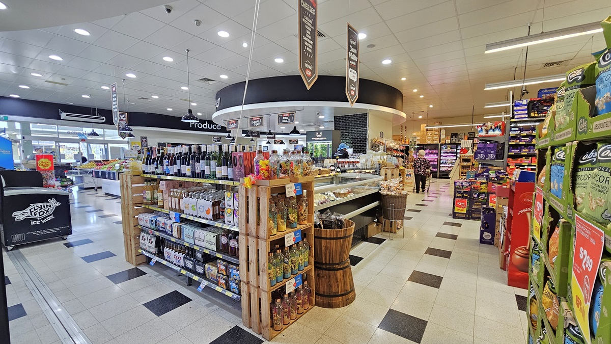 A closer look at a Grocery Aisle inside the Tweed Valley IGA. A three-layer shelf filled with wines and liquors is visible near the wooden buckets and the displayed delicacies. On the right, groceries like popcorn, sweets, and chips are neatly organized. On the left, a black freezer with “flying fox” written in it is noticeable. A closer look at a Grocery Aisle inside the Tweed Valley IGA. A three-layer shelf filled with wines and liquors is visible near the wooden buckets and the displayed delicacies. On the right, groceries like popcorn, sweets, and chips are neatly organized. On the left, a black freezer with “flying fox” written in it is noticeable.