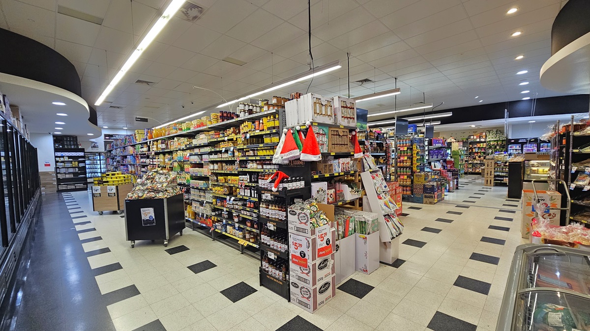 A closer look at the pathways beside the grocery aisles. Santa hats are visibly placed above layers of liquors beside the Christmas wrapping paper and other Christmas decorations. Two box trolleys with sweets and other products are apparent on the left. On the pathway on the right, a trolley with products is noticeably placed near a freezer and a multi-layer rack. A closer look at the pathways beside the grocery aisles. Santa hats are visibly placed above layers of liquors beside the Christmas wrapping paper and other Christmas decorations. Two box trolleys with sweets and other products are apparent on the left. On the pathway on the right, a trolley with products is noticeably placed near a freezer and a multi-layer rack.