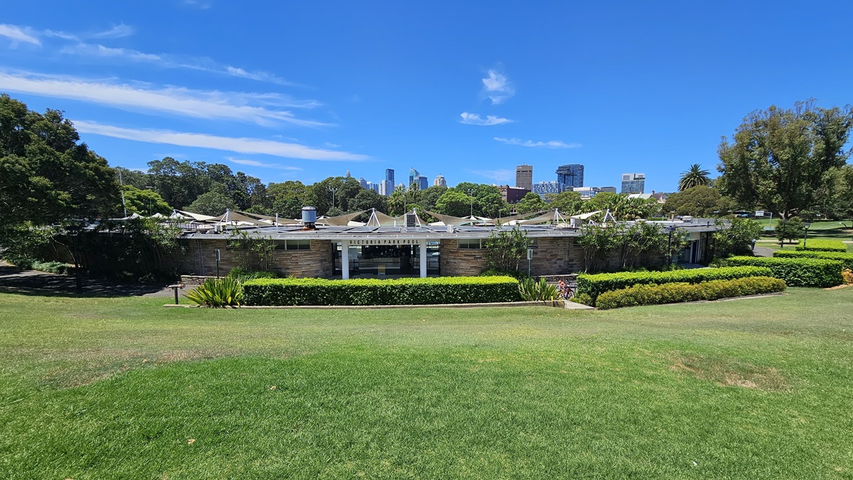 The building is a low-rise modern brick structure with multiple shade cloths at the back. Surrounding the building are landscape shrubs, ornamental plants, and neatly trimmed grass. Further ahead, tall trees and commercial buildings come into view. The building is a low-rise modern brick structure with multiple shade cloths at the back. Surrounding the building are landscape shrubs, ornamental plants, and neatly trimmed grass. Further ahead, tall trees and commercial buildings come into view.