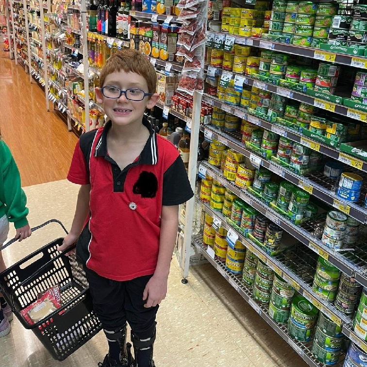 A boy with glasses in a red and black polo shirt is standing in a grocery aisle.