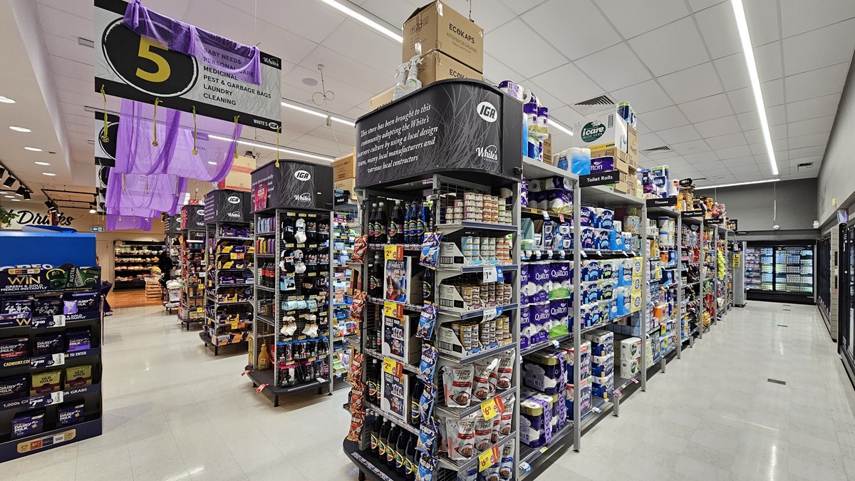 A supermarket aisle with a white tiled floor. On the left, there are shelves stocked with cleaning products and a large black sign with a yellow number 5. In the middle, there are displays of various household items, including light bulbs and batteries. The ceiling is white with rectangular fluorescent lights. On the right, there are shelves filled with toilet paper and paper towels. The background features more aisles and a refrigerated section with glass doors. A supermarket aisle with a white tiled floor. On the left, there are shelves stocked with cleaning products and a large black sign with a yellow number 5. In the middle, there are displays of various household items, including light bulbs and batteries. The ceiling is white with rectangular fluorescent lights. On the right, there are shelves filled with toilet paper and paper towels. The background features more aisles and a refrigerated section with glass doors.