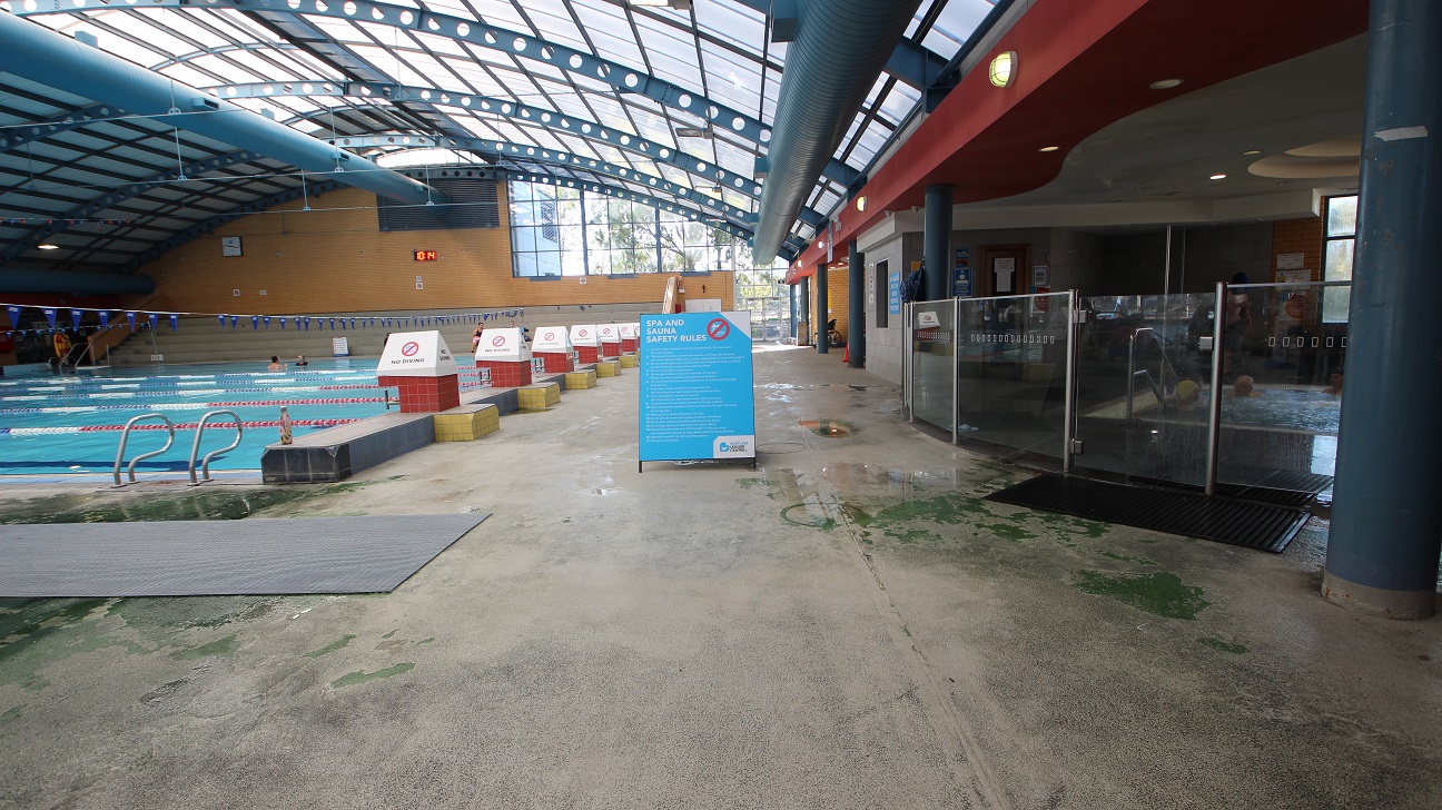 The image shows the 8-lane 25m lap pool on the left side while the jacuzzi can be found on the right side, separated by the hip-length glass walls. The lanes are separated by white, red, and blue floating lane ropes. Small triangular flags placed horizontally in the pool area can be seen hanging 5 meters from the water's surface. On the red elevated section, the right side of the pool, are triangular white signboards cautioning swimmers that no diving is allowed. The image shows the 8-lane 25m lap pool on the left side while the jacuzzi can be found on the right side, separated by the hip-length glass walls. The lanes are separated by white, red, and blue floating lane ropes. Small triangular flags placed horizontally in the pool area can be seen hanging 5 meters from the water's surface. On the red elevated section, the right side of the pool, are triangular white signboards cautioning swimmers that no diving is allowed.