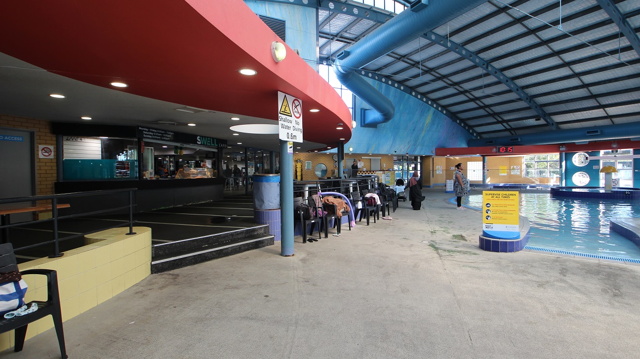 The seating area outside the Swell Café is near the children’s pool at the Aquatic centre in Whitlam Leisure Centre. The left side of the café is a brick wall and the door which can only be accessed by staff members. The ceiling is painted with grey and red paint with peculiar fluorescent sizes. The seating area outside the Swell Café is near the children’s pool at the Aquatic centre in Whitlam Leisure Centre. The left side of the café is a brick wall and the door which can only be accessed by staff members. The ceiling is painted with grey and red paint with peculiar fluorescent sizes.