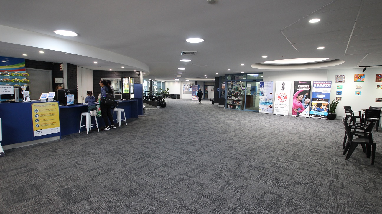 Next to the curvy reception tables is a thigh-light counter table with tall white bar stools. Heading towards the right from the reception desk are the Health Club and Swell Café. Different wall paintings and posters displayed near the wall can be seen opposite the reception area as well as black chairs and tables. Next to the curvy reception tables is a thigh-light counter table with tall white bar stools. Heading towards the right from the reception desk are the Health Club and Swell Café. Different wall paintings and posters displayed near the wall can be seen opposite the reception area as well as black chairs and tables.