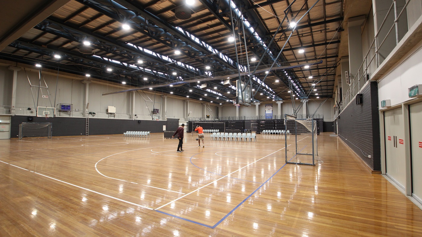 The Stadium is two basketball courts in size and has highly polished timber flooring, with a brown ceiling with dark beams including fluorescent lights. Underneath the basketball rings are football nets. Scattered on the other side of the basketball court are white chairs. The lower part of the walls are made of black bricks. The second floor with handrails can be accessed by a metal ladder. The Stadium is two basketball courts in size and has highly polished timber flooring, with a brown ceiling with dark beams including fluorescent lights. Underneath the basketball rings are football nets. Scattered on the other side of the basketball court are white chairs. The lower part of the walls are made of black bricks. The second floor with handrails can be accessed by a metal ladder.